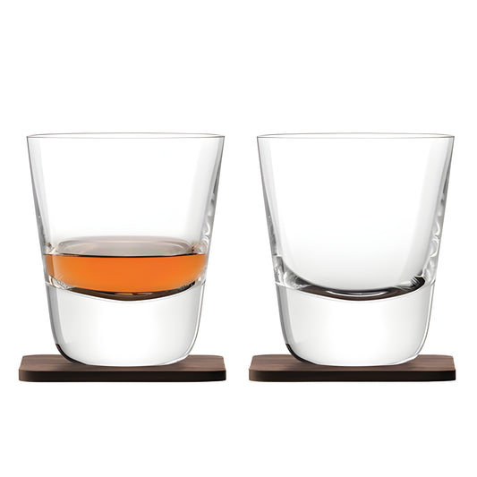Two crystal whisky tumblers on wooden coasters, one glass filled with whisky.